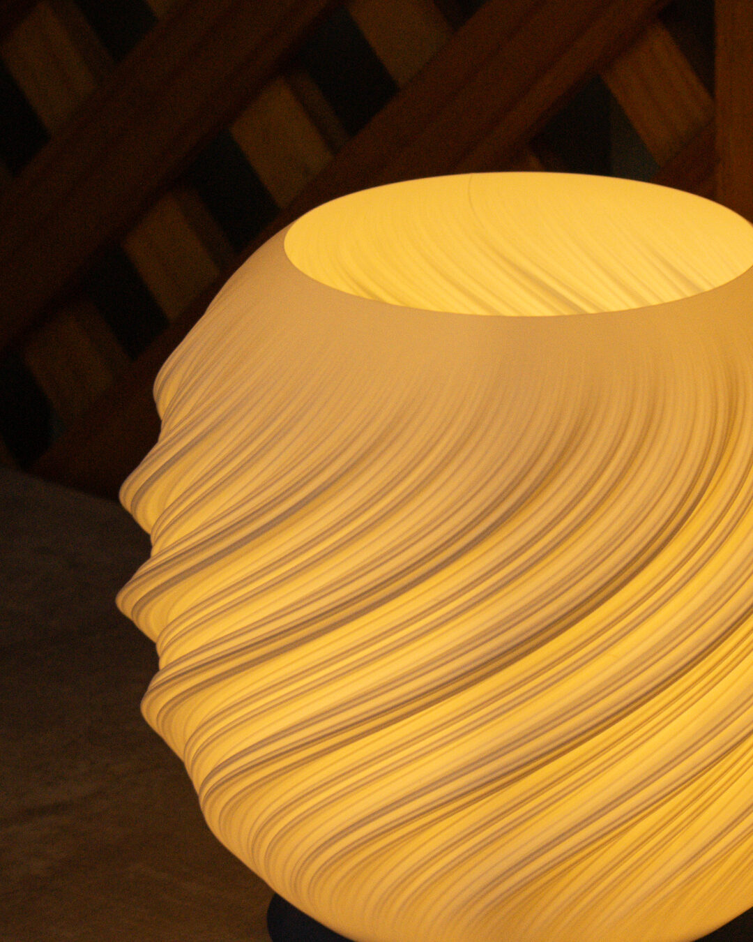 Detalhe das camadas em espiral impressas em 3D da luminária Aura acesa